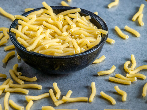 Closeup of Italian food yellow raw uncooked vermicelli, macaroni, noodle, pastry, pasta isolated dark bowl (close-up,meal, cuisine, cooking, gray, dry, dish, studio, plate, dinner, tile, cement)
