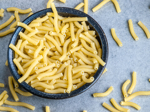 Closeup of Italian food yellow raw uncooked vermicelli, macaroni, noodle, pastry, pasta isolated dark bowl (close-up,meal, cuisine, cooking, gray, dry, dish, studio, plate, dinner, tile, cement)
