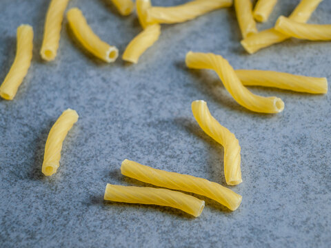 Closeup of Italian food yellow raw uncooked vermicelli, macaroni, noodle, pastry, pasta isolated dark cement table (close-up, cuisine, cooking, gray, dry, dish, studio, plate, dinner, tile, cement)
