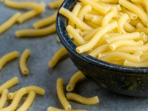Closeup of Italian food yellow raw uncooked vermicelli, macaroni, noodle, pastry, pasta isolated dark bowl (close-up,meal, cuisine, cooking, gray, dry, dish, studio, plate, dinner, tile, cement)
