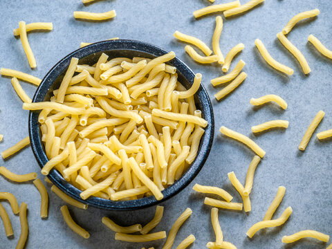 Scattered Macaroni Pasta in a Black Bowl - Closeup of Italian food yellow raw uncooked vermicelli, macaroni, noodle, pastry, pasta isolated dark bowl