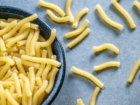Closeup of Italian food yellow raw uncooked vermicelli, macaroni, noodle, pastry, pasta isolated dark bowl (close-up,meal, cuisine, cooking, gray, dry, dish, studio, plate, dinner, tile, cement)
