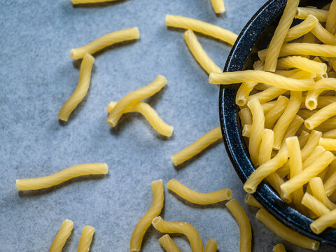 Closeup of Italian food yellow raw uncooked vermicelli, macaroni, noodle, pastry, pasta isolated dark bowl (close-up,meal, cuisine, cooking, gray, dry, dish, studio, plate, dinner, tile, cement)
