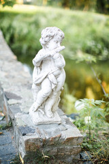 Fototapeta na wymiar The cute stone statue playing flute instrument in the garden. Angel sculpture