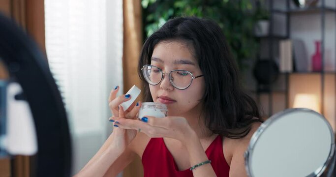 Influencer blogger talks about skin care. Woman recording video blog with phone as she applies moisturizer to face. A girl talks about beauty treatments.