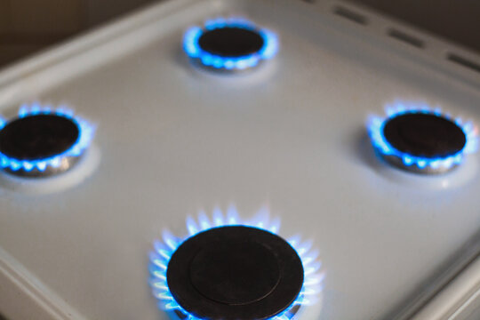 Four gas burners burn with blue flames on a white kitchen stove