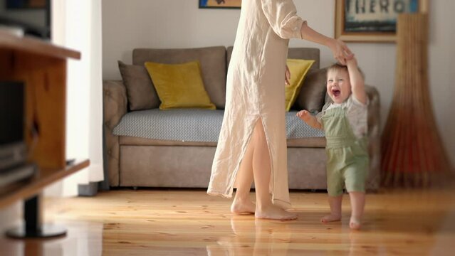 Little feet walking floor. Baby learning walk home. Baby first steps. Affectionate family cute adorable funny little kid boy embrace kiss young mom, happy loving mother and small child