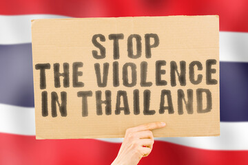 The phrase " Stop the violence in Thailand " is on a banner in men's hands with a blurred Thai flag in the background. Sad. Rights. Security. Social. Stress. Combat. Hate. Cruelty. Furious