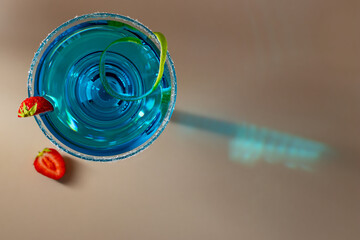 Glass with blue margarita cocktail garnished with lime zest and strawberries