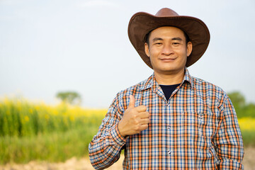 Portrait of handsome Asian man farmer is at garden, wears hat, plaid shirt, thumbs up. Concept :...
