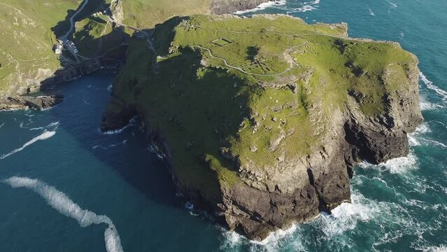 Aerial drone shot of Tintagel, rugged and rocky stretch of coastline with cliffs and rough seas, Cornwall, South West England