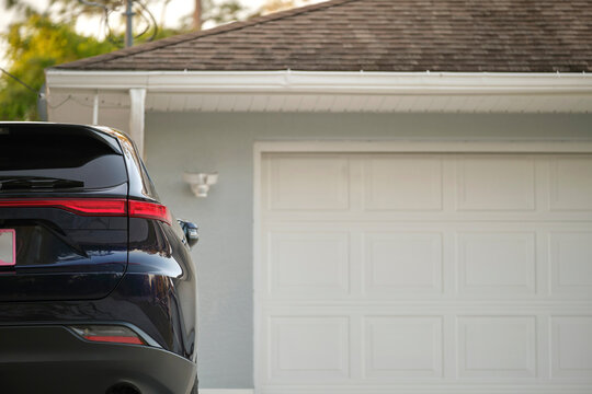 Car Parked In Front Of Wide Garage Double Door On Concrete Driveway Of New Modern American House