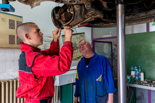 A senior experienced technician helps a young fellow mechanic to do disc replacement at workshop garage