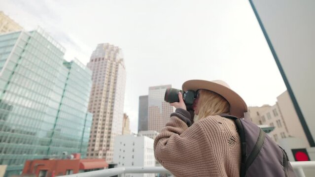 Female tourist shooting skyscrapers below cloudy skyline while standing on a rooftop. Modern architecture of a financial district with glass facades of the buildings. High quality 4k footage