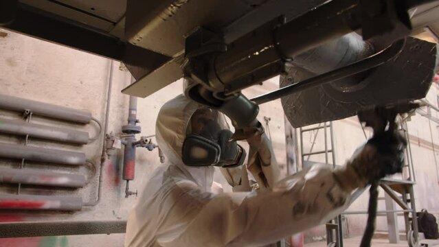 Close-up of the face of a woman in a mask with a respirator who works in the paint shop. She paints the metal structure of the train with gray paint from a spray gun to reduce corrosion