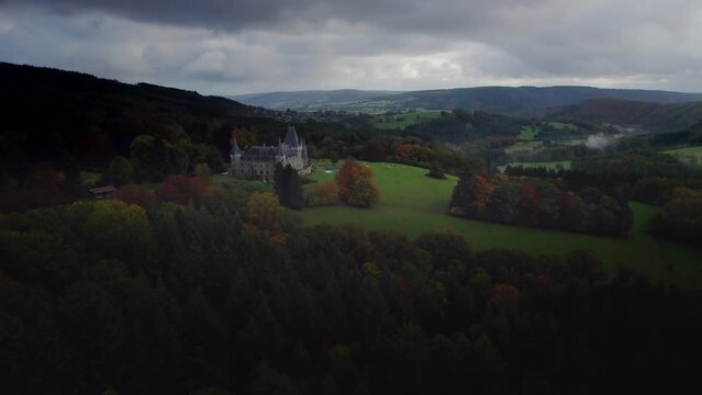 Beautiful hotel castle Chateau de Froidcour, in the middle of the Belgian Ardennes, surrounded by autumn forests and meadows with cows. Belgium Ardennes Aerial view establishing shot of the castle 