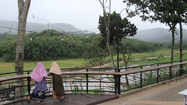 Two women wearing hijab while enjoying the resort atmosphere with views of rice fields and forests