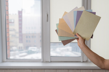 Woman holding fabric samples of roller blinds against window background. 