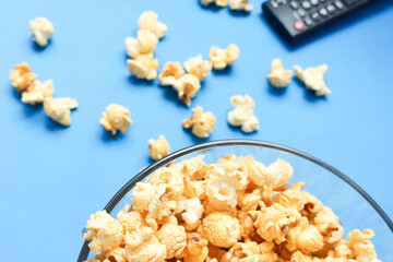 Obraz na płótnie Canvas Delicious caramel popcorns sweet dessert on blue background, snacks in a glass bowl for favorite movie times.
