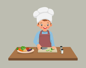 cute little boy chef cooking meal cutting slicing cucumber vegetable with knife in the kitchen