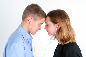 Teenager boy and girl listen to music from one earphone with their eyes closed head-on on a white background. First love concept. Studio photography.