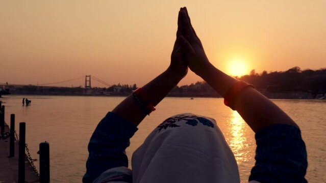 young indian girl praying the holy ganges river and sun setting at horizon at river bank