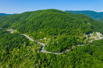 Winding road is meandering between blue sea and green mountains. Aerial view of car driving along...