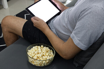 Obraz na płótnie Canvas Glass cup with salted popcorn & digital tablet in a gray armchair.