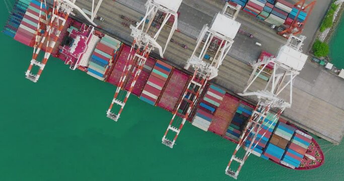 Aerial top view of cargo vessel ship loading and unloading in deep sea port. Modern industrial shipyard with shipping containers being loaded onto a freight ship, import export and global supply chain