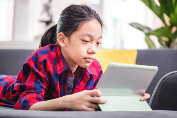 Happy child with digital tablet while resting on sofa, Asian kid girl in living room