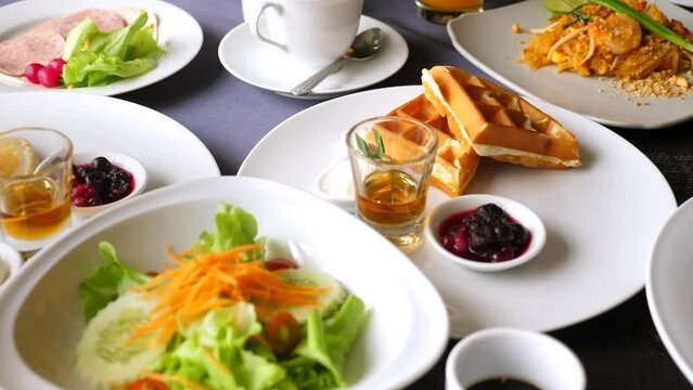 Breakfast in hotel or resort. Thai cuisine. Close-up view of food on table in restaurant or cafe. Coffee cup, orange juice, pancakes, waffles, salad, cold cut. Lunch, branch or dinner concept.