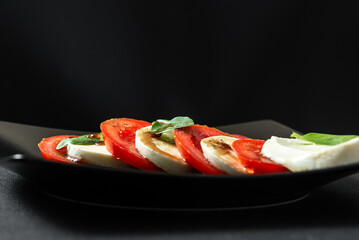 Fresh italian caprese salad with mozzarella and tomatoes on dark plate. Italian salad on a black...