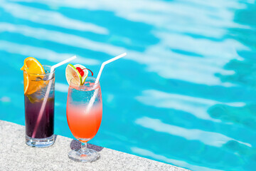Two cocktails at swimming pool in luxurious hotel at sunny summer day. Mocktail drinks with straws at poolside in luxury tropical resort. Travel, vacations, holidays or tourism concept. Copy space.