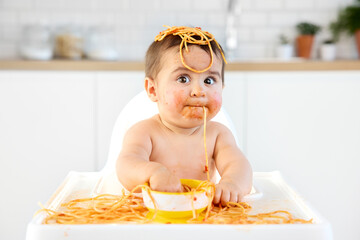 Funny baby with spaghetti hanging from mouth
