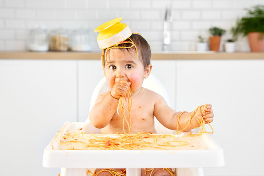Funny messy baby with bowl of spaghetti on top of head