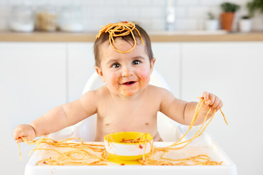 Happy baby eating spaghetti with his hands