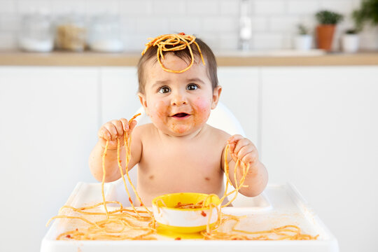 Messy baby eating spaghetti with his handsv