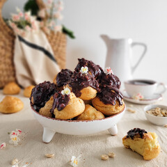 Chocolate profiteroles with custard in a white plate decorated with flowers.
Homemade custard cakes are decorated with chocolate icing with nuts and flowers.

