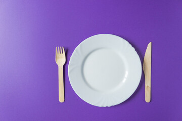 Tableware from natural materials - bamboo wooden fork and knife with white plate isolated on a very peri background.