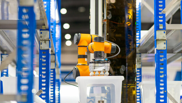  Smart warehouse concept: The COBOT (Collaborative Robot) with gripper is automatically picking plastic box from shelf in warehouse.