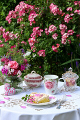 Tischdekoration mit Stück Kuchen, Porzellan und Blumenstrauß im Sommergarten