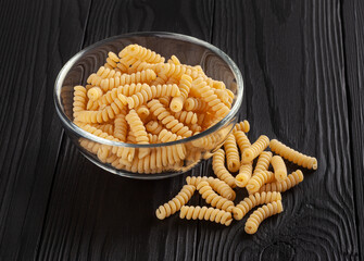 Uncooked fusilli pasta in glass bowl on black wooden background