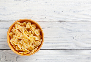 Uncooked farfalle rigate pasta in wooden bowl on white wooden background