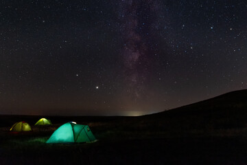 Travel and camping concept - three glowing camping tents at night under a starry sky with milky way...