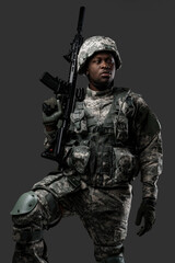 Combative african soldier with serious face holding rifle looking away against dark background.