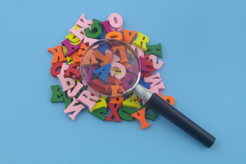 Education review concept. Many wooden English letters and magnifying glass on blue background close up.