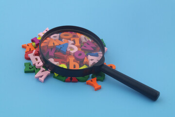 Education review concept. Many wooden English letters and magnifying glass on blue background close...