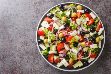 Fototapeta na wymiar Classic Greek salad from tomatoes, cucumbers, onion with olives, oregano and feta cheese close-up in a plate on the table. Horizontal top view from above