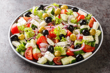 Healthy greek salad of fresh vegetables with tomatoes, lettuce, cucumbers, olives, feta cheese in plate on gray stone background. Healthy food, vegetarian dieting, close up