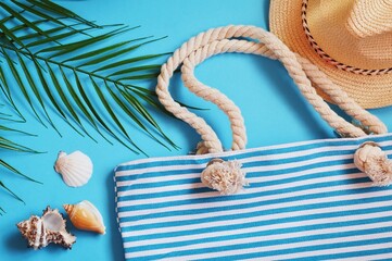 International sea travel 2022 flat lay photo. Palm leaves, striped bag, straw hat and seashells on a blue background. Summer beach accessories top view. Image for design website
